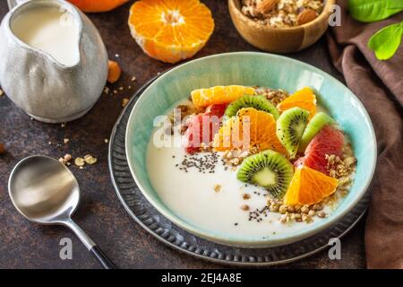 Gesundes Frühstück. Schüssel mit hausgemachtem Müsli mit Joghurt, frischem Obst, Nüssen und Chiasamen auf einer Tischplatte aus dunklem Stein. Stockfoto
