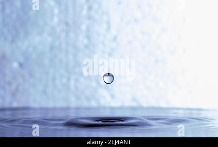 Wassertropfen steigt nach dem Fallen auf blaue Wasseroberfläche Stockfoto