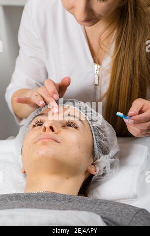 Kosmetikerin oder Dermatologin, die Creme mit der Hand auf das Gesicht während der Gesichtsmassage für eine entspannte junge Frau im Schönheitssalon, Rückansicht. Stockfoto