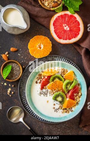 Gesundes Frühstück. Schüssel mit hausgemachtem Müsli mit Joghurt, frischem Obst, Nüssen und Chiasamen auf einer Tischplatte aus dunklem Stein. Draufsicht flach liegend. Stockfoto