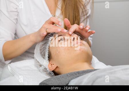 Kosmetikerin oder Dermatologin, die Creme mit der Hand auf das Gesicht während der Gesichtsmassage für eine entspannte junge Frau im Schönheitssalon, Rückansicht. Stockfoto