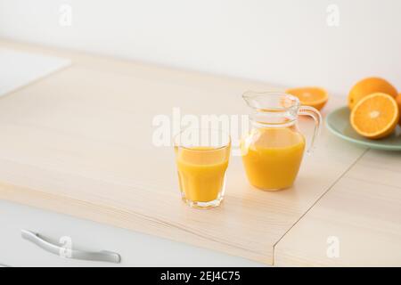 Frisch gepresster Orangensaft aus Glas und Krug, Obst auf Teller auf weißen Möbeln in moderner minimalistischer Küche Stockfoto