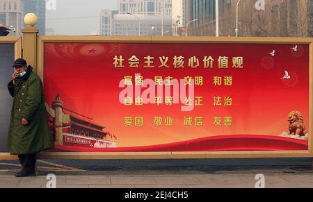 Peking, China. Februar 2021, 21st. Ein Chinese raucht eine Zigarette neben einem Regierungsbanner, das die Tugenden der "Sozialistischen Grundwerte" von gleicher Gerechtigkeit, Rechtsstaatlichkeit, patriotischer Gesinnung und freundschaftlichem sein am Sonntag, dem 21. Februar 2021 in einem Einkaufszentrum in der Innenstadt Pekings preist. Die Regierung Chinas ist kollektiv ein Staat der Autorität unter der Führung der Kommunistischen Partei Chinas (KPCh), der die chinesischen Bürger ermutigt, die Gebote des Sozialismus und Kommunismus zu befolgen. Foto von Stephen Shaver/UPI Kredit: UPI/Alamy Live Nachrichten Stockfoto