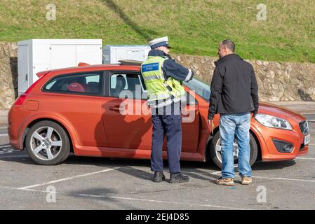 Southend on Sea, Essex, Großbritannien. Februar 2021, 21st. Das warme und sonnige Wetter hat die Menschen trotz der COVID 19-Sperrwarnungen an die Küste von Southend on Sea gebracht. Der Parkplatz am Meer wurde geschlossen, Polizei und Aufseher patrouillierten, um sich zu bewegen oder stoppte Autos auszustellen. Fahrer, der zum Auto zurückkehrt, nachdem er ein Ticket ausgestellt hat und mit dem Beamten der Zivilbehörde, dem Verkehrsaufseher, gesprochen hat Stockfoto