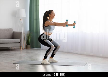 Sportliche junge Frau macht Kniebeugen mit Hanteln zu Hause Stockfoto
