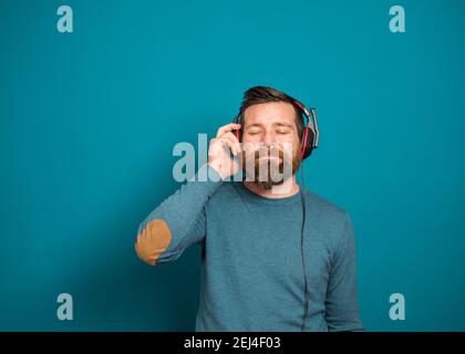 Junger Mann über isolierter blauer Wand, der Musik mit hört Kopfhörer Stockfoto