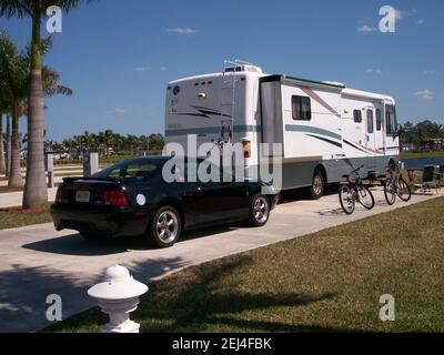 Wohnmobil parkt in einem modernen Wohnmobil-Resort in sonnigem, warmem Klima. Schwarzes Auto parkte hinter dem Wohnmobil in der Nähe von Fahrrädern. Stockfoto