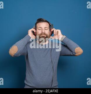 Junger Mann über isolierter blauer Wand, der Musik mit hört Kopfhörer Stockfoto
