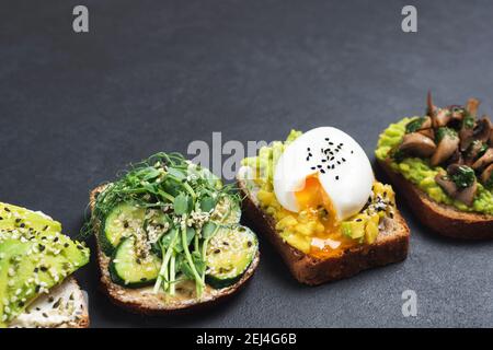 Gesunde vegetarische Toasts mit Avocado und verschiedenen Belägen auf schwarzem Hintergrund, Kopierraum Stockfoto
