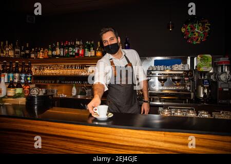 Barkeeper arbeitet mit einer Maske, um sich vor der zu schützen Coronavirus und serviert dem Kunden einen italienischen Kaffee Stockfoto