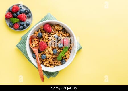 Granola in Schale mit frischen Beeren auf gelbem Hintergrund, Draufsicht. Gesundes Frühstückscerealien Stockfoto