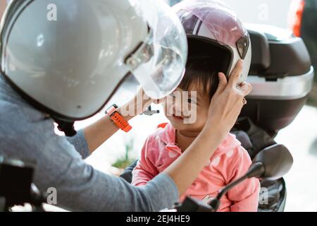 Das Baby trägt einen Motorradhelm, wenn die Mutter hilft Er auf dem Motorrad Stockfoto