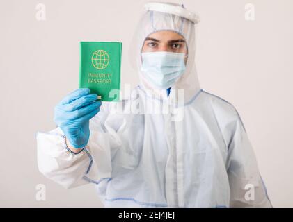 Medizinischer Spezialist in schützenden Biohazard Kostüm zeigt Coronavirus Immunität Pass Auf hellem Studiohintergrund Stockfoto