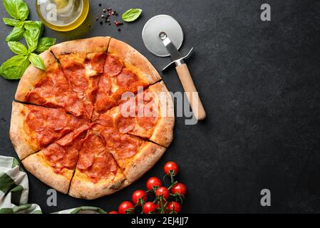 Hot Pepperoni Pizza Auf Schwarzem Beton Hintergrund Mit Pizza Cutter, Basilikum Blatt Und Kirschtomaten Auf Der Seite. Draufsicht. Deleive Pizza, Platz Kopieren Für Stockfoto