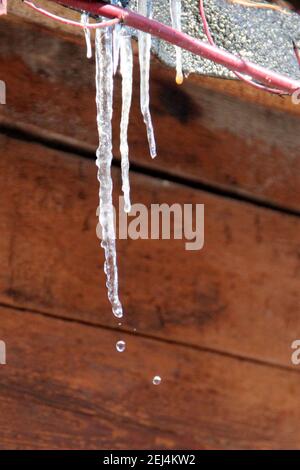 Eiszapfen hängen vom Dach der Holzkonstruktion. Stockfoto