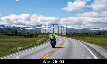 Motorradfahrer auf der Straße durch Tundra, Landstraße, Dovrefjell Nationalpark, Oppdal, Norwegen Stockfoto