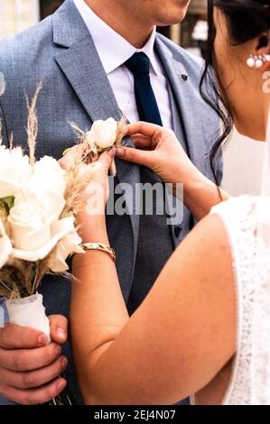 Die Braut legt am neuen Hochzeitstag einen Boutonniere auf die Jacke des Bräutigams. Stockfoto