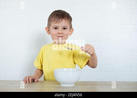 Kleiner Linkshänder Junge in einem gelben T-Shirt essen Obstsalat und lächeln. Kinder gesunde Ernährung Konzept. Ernährungsprodukte. Gesundheitswesen Stockfoto