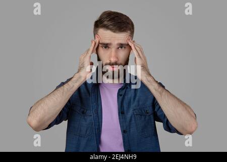 Junger Mann mit schrecklichen Kopfschmerzen, leiden an Migräne auf grauen Studio-Hintergrund Stockfoto