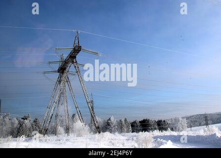 Eine unglaubliche Kombination aus der Stahlstruktur des Powerline Pylons mit gestreckten Drähten im Vordergrund und dem Winterwald am Horizont. Stockfoto