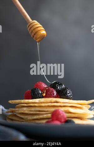 Gießen von rohem Honig über hausgemachte Crepes auf dem Tisch, dunkle Lebensmittel Fotografie Stockfoto