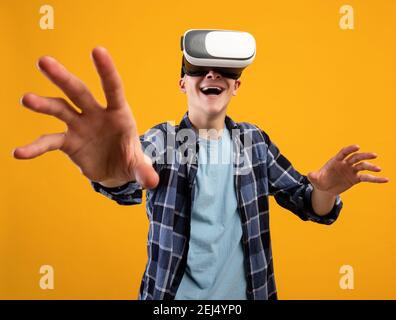 Aufgeregt jungen Kerl erleben virtuelle Realität in VR-Headset, die Steuerung Gesten auf orangenen Hintergrund Stockfoto
