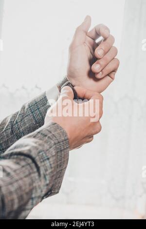 Morgen des Bräutigams, Details und Ehemannstreffen am Hochzeitstag. Der Mensch stellt eine Uhr an der Hand auf einen weißen Hintergrund 2021. Stockfoto