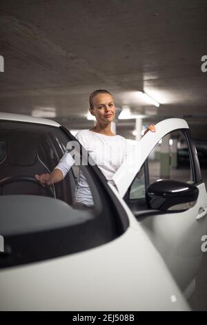 Tiefgarage/Garage (flaches DOF; farbiges Bild) - junge Frau mit ihrem Auto in der Tiefgarage Stockfoto