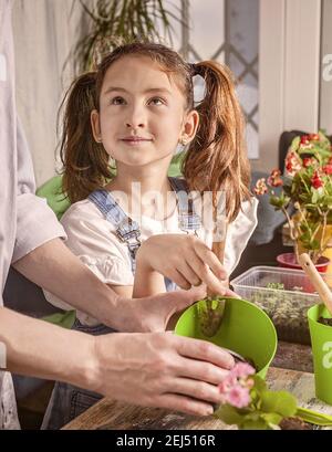 Schönes lächelndes kaukasisches Mädchen hilft ihrer Mutter, Blumen zu Pflanzen. Gartenarbeit für zu Hause. Glückliche Kindheit, positive Emotionen. Vertikale Aufnahme. Stockfoto