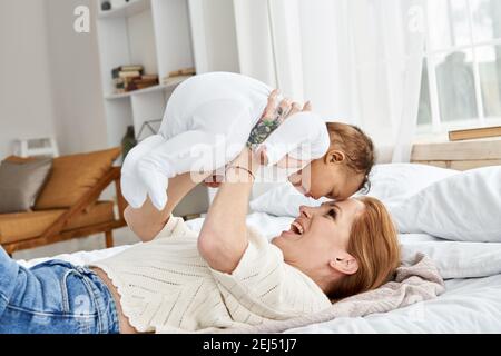 Glücklich kaukasische Mutter mit Spaß Heben niedlichen kleinen Baby Tochter im Bett. Stockfoto