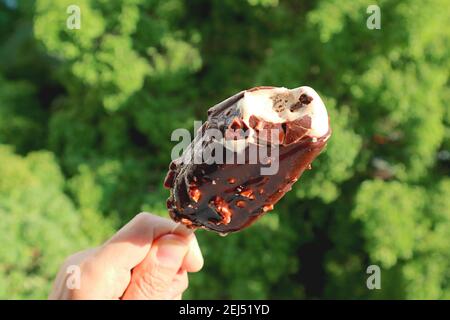 Nahaufnahme eine schmelzende, in Schokolade getauchte Eiscreme-Bar in der Hand An einem sonnigen Tag Stockfoto