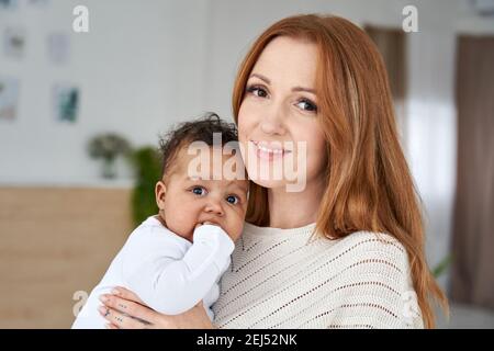 Glücklich junge kaukasische Mutter hält niedlich afrikanisch amerikanisch Baby Tochter. Hochformat Stockfoto