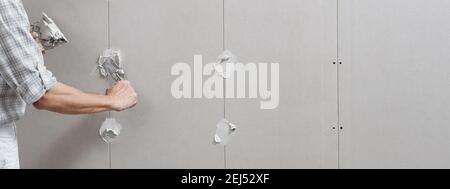 Nahaufnahme Hände Mann Trockenbau Arbeiter oder Gipser setzen Stuck auf Gipskartonwand mit einer Kelle und einem Spachtel, füllen Sie die Schraubenlöcher, Panoramabild Stockfoto