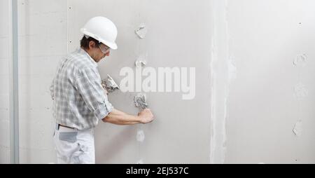 Mann Trockenbau Arbeiter oder Gipser Gips auf Gipskartonwand mit einer Kelle und einem Spachtel, füllen Sie die Schraubenlöcher, tragen weißen Hardhut und saf Stockfoto