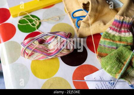 Wollknäuel auf einem Tisch sitzend mit Stricknadeln, teilweise gestrickte Socke, Bastelgarn, die warme Wollsocken aus Handarbeit während der covid Pandemie UK machen Stockfoto