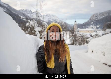 Ein afrikanisches Mädchen, das stark bekleidet ist, um der Kälte zu widerstehen, posiert in der Nähe einer Schneemauer in den Bergen. Stockfoto