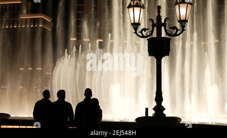 LAS VEGAS, NEVADA USA - 13 DEC 2019: Leute, die Bellagio Brunnen musikalische Leistung in der Nacht betrachten. Kontrastierende Silhouetten und leuchtendes Tanzen Stockfoto