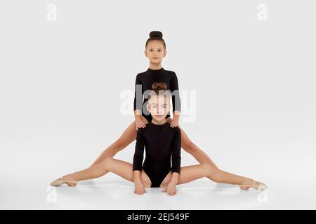 Zwei niedliche Turnerin Kind Mädchen zeigen sportliche Fähigkeiten auf weißem Studio Hintergrund. Querfaden Stockfoto