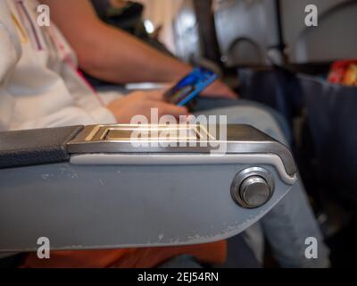 Nahaufnahme eines runden Metallknopfes auf einer abgenutzten Armauflage, um zurückzufallen und sich an einem Flugzeug zu erholen. Person sitzt in einem Passanten Sitz und holdin Stockfoto