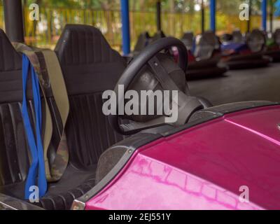 Nahaufnahme eines Rades und zwei Sitze eines elektrischen altmodischen Stoßfängers und einer Reihe von Autos, die hinter in einem städtischen Vergnügungspark stehen. Spaß für die ganze Familie. Stockfoto