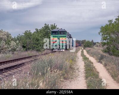 Ein langer Güterzug, der an einem heißen, sonnigen Sommertag entlang der ländlichen Eisenbahn des Landes fährt. Retro altmodischen Stil Motor und Wagen. Stockfoto