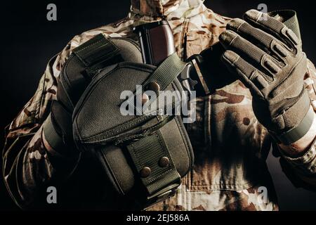 Foto von Soldat in Tarnuniform und taktische Handschuhe halten Pistole Holster auf schwarzem Hintergrund. Stockfoto