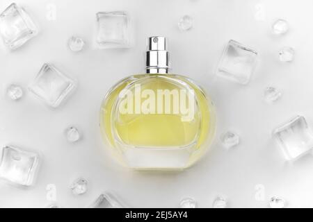 Weibliche Parfüm gelbe Flasche, objektive Foto von Parfüm-Flasche in Eiswürfeln und Wasser auf weißem Tisch. Blick von oben. Modellbild Produktfoto, Kontra Stockfoto