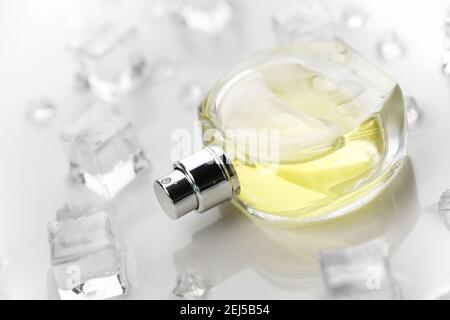 Weibliche Parfüm gelbe Flasche, objektive Foto von Parfüm-Flasche in Eiswürfeln und Wasser auf weißem Tisch. Blick von oben. Modellbild Produktfoto, Kontra Stockfoto