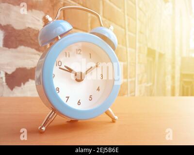 Kleiner blauer Wecker auf rotem Backsteinmauer Hintergrund in der Morgensonne. Stockfoto