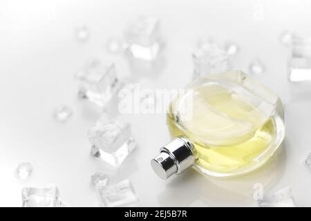 Weibliche Parfüm gelbe Flasche, objektive Foto von Parfüm-Flasche in Eiswürfeln und Wasser auf weißem Tisch. Blick von oben. Modellbild Produktfoto, Kontra Stockfoto