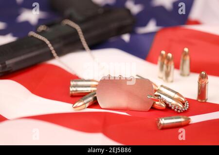 Viele gelbe 9mm Kugeln und Pistole mit Dogtags auf der Flagge der Vereinigten Staaten. Konzept von Dienst und Dienst in US-Armee-Truppen. Veteranenkonzept Stockfoto