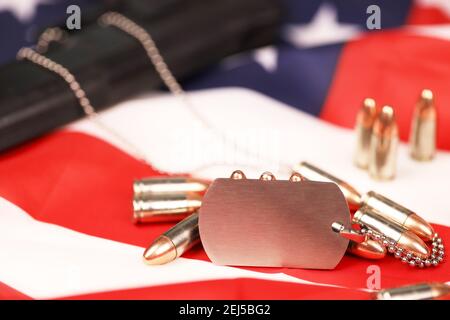 Viele gelbe 9mm Kugeln und Pistole mit Dogtags auf der Flagge der Vereinigten Staaten. Konzept von Dienst und Dienst in US-Armee-Truppen. Veteranenkonzept Stockfoto