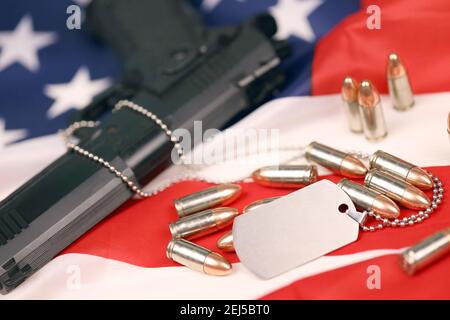 Viele gelbe 9mm Kugeln und Pistole mit Dogtags auf der Flagge der Vereinigten Staaten. Konzept von Dienst und Dienst in US-Armee-Truppen. Veteranenkonzept Stockfoto