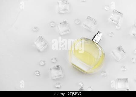 Weibliche Parfüm gelbe Flasche, objektive Foto von Parfüm-Flasche in Eiswürfeln und Wasser auf weißem Tisch. Blick von oben. Modellbild Produktfoto, Kontra Stockfoto